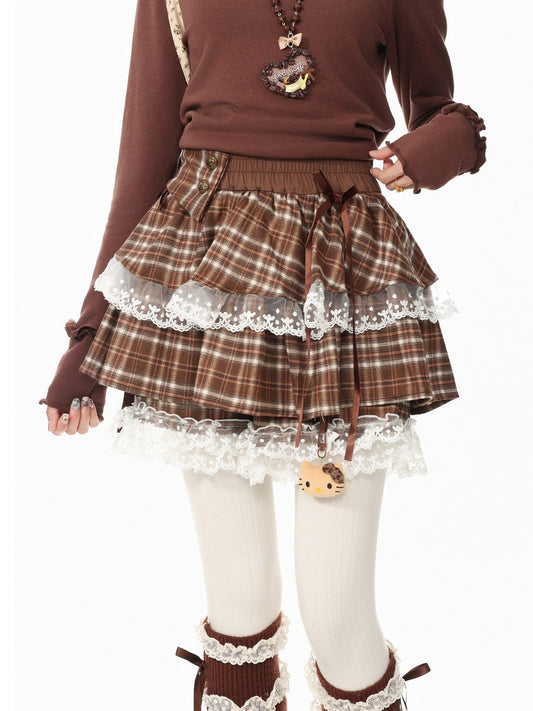 A person wearing a brown long-sleeve top, a brown plaid tiered skirt with white lace trim, white tights, and brown lace-up boot covers, photographed against a plain white background.