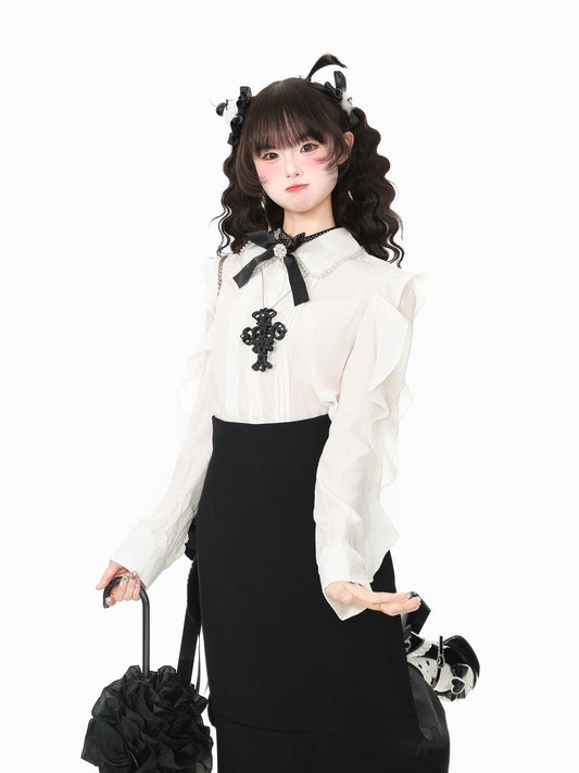A young woman modeling a black and white gothic Lolita outfit, featuring a white long-sleeve blouse with a black bow and cross embellishment, a black skirt, and matching black hair accessories, set against a plain white background.