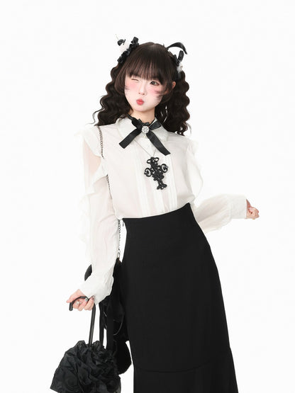 A model posing in a white long-sleeve blouse with a black bow and black lace applique, paired with a black skirt, holding a black ruffled handbag against a plain white background.