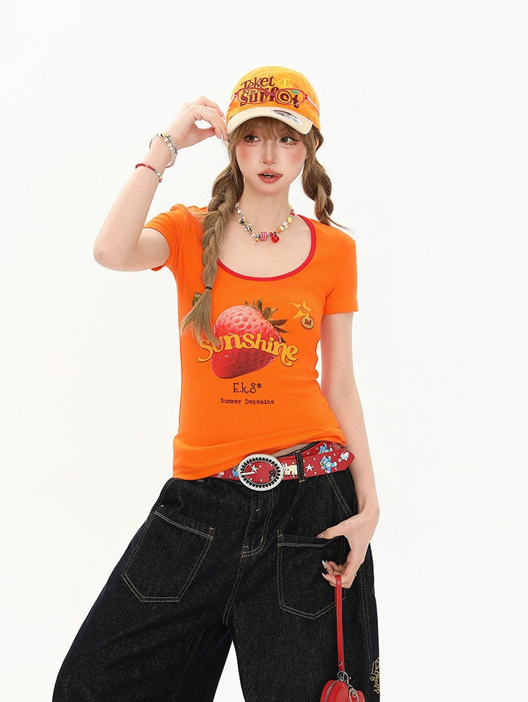 Person wearing an orange t-shirt with a graphic design and a cap, standing against a white background.