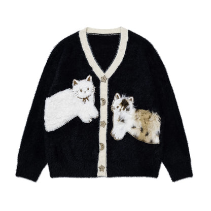 A black fuzzy cardigan sweater with cream-colored trim and two large cat appliqués on the front, one white cat and one calico cat, shown on a plain white background.