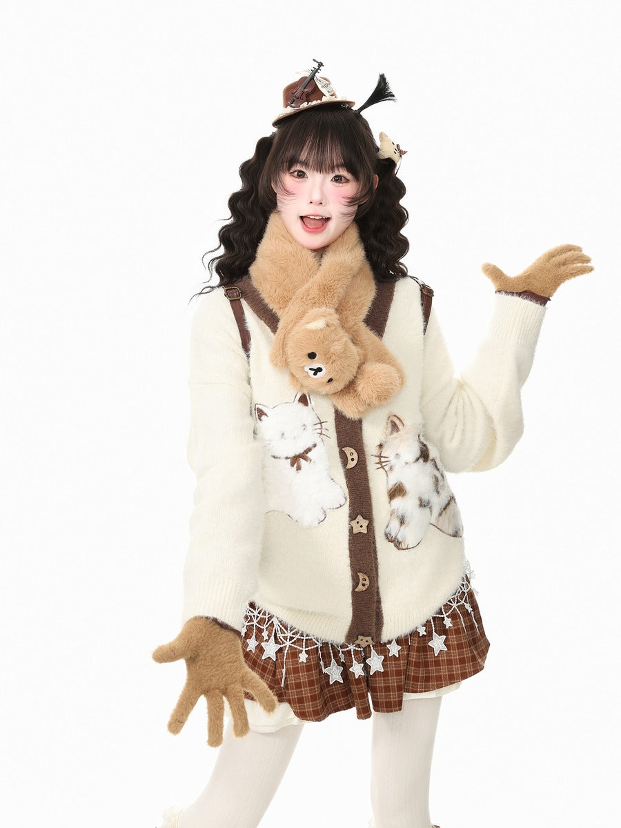 A young woman modeling a cozy, cat-themed winter outfit against a solid white background. The outfit includes a cream-colored knit cardigan decorated with white cat illustrations and brown accents, a brown plaid mini skirt, a fluffy brown faux-fur scarf, and matching brown gloves.
