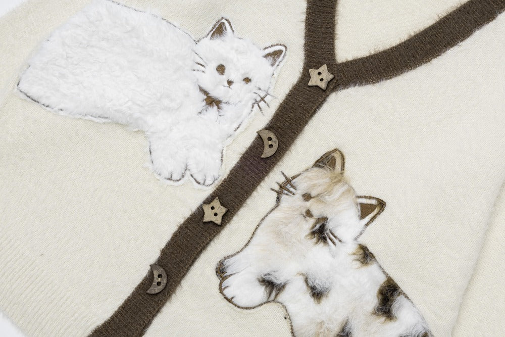 Close-up of a cream-colored knit sweater featuring two embroidered cats and a dark brown branch design with small star and crescent embellishments.