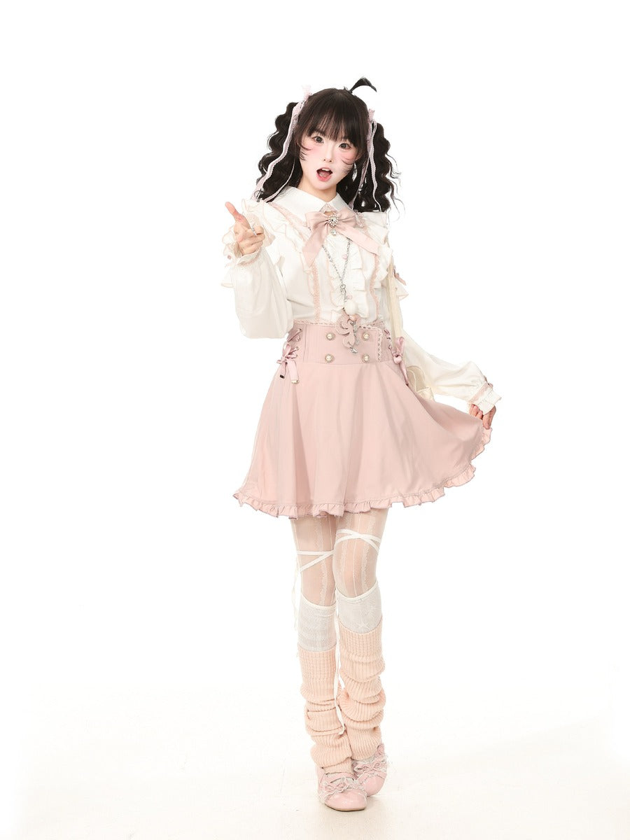 A young woman modeling a Lolita-style outfit consisting of a cream ruffled blouse, a light pink pleated mini skirt with decorative buttons, matching pink and cream thigh-high stockings, and pink lace-up shoes, set against a plain white studio background.