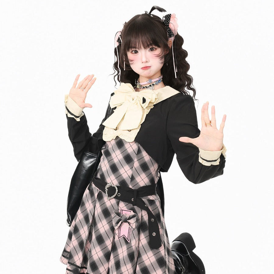 A model posing in a black and pink plaid lolita dress with a large cream bow, black cropped jacket, and black boots against a plain white background.
