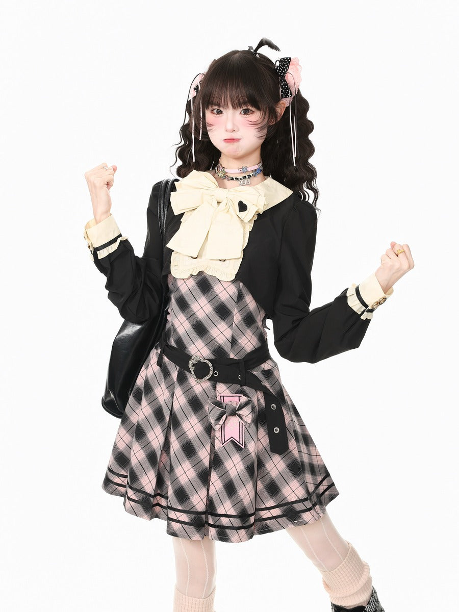 A young woman modeling a schoolgirl-style outfit with a black cardigan, cream ruffled collar, pink and black plaid pinafore dress, black belt, and cream knee socks against a plain white background.