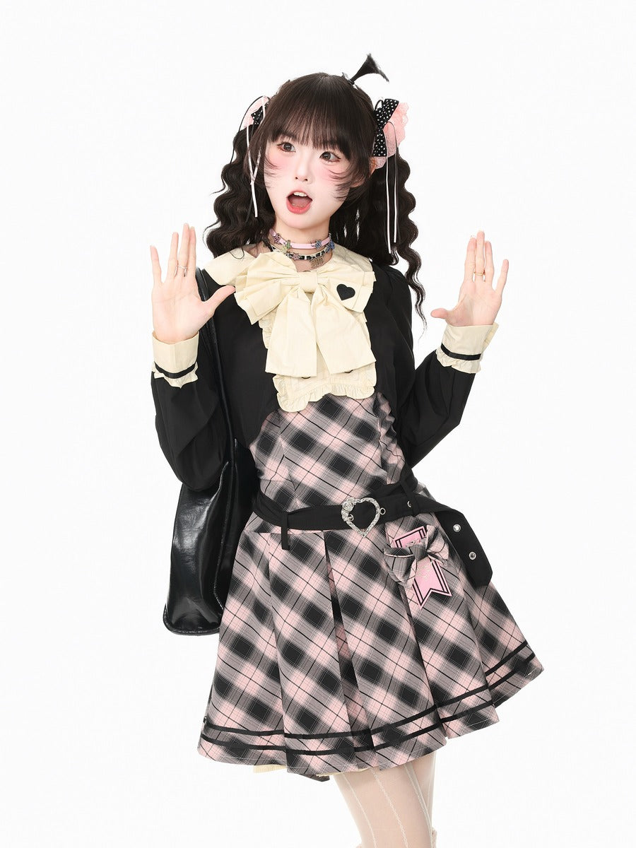A young woman posing in a black and pink plaid schoolgirl-style outfit with a cream bow collar, black jacket, and black skirt, set against a plain white background.
