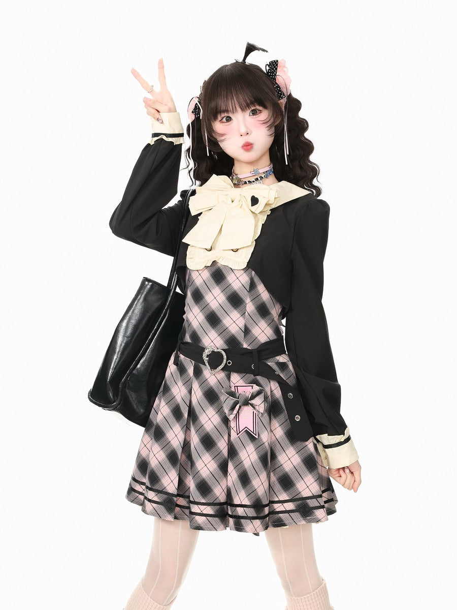 A young woman posing in a schoolgirl-style outfit featuring a black cardigan, a pink and black plaid pinafore dress, a large cream bow, and a black choker, set against a plain white background.