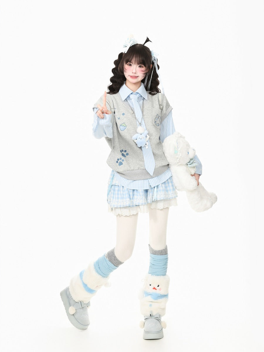 A young girl models a cute, pastel-themed outfit consisting of a light blue and white plaid mini skirt, a gray vest with blue paw prints, a striped shirt, and matching accessories, while holding a white plush toy against a solid white background.