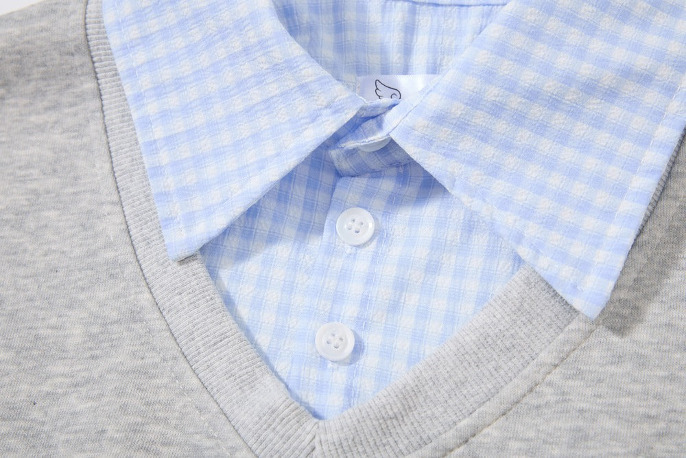 Close-up of a light blue and white gingham dress shirt layered under a gray v-neck knit sweater, showing the collar, buttons, and ribbed neckline.