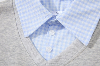 Close-up of a light blue and white gingham dress shirt layered under a gray v-neck knit sweater, showing the collar, buttons, and ribbed neckline.