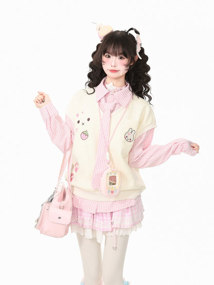 A young woman modeling a cute, pastel-themed outfit consisting of a cream-colored vest with cartoon rabbit and strawberry patches, a pink and white gingham long-sleeve shirt, a matching pink and white gingham pleated skirt, white thigh-high stockings, and a small pink shoulder bag, set against a plain white background.