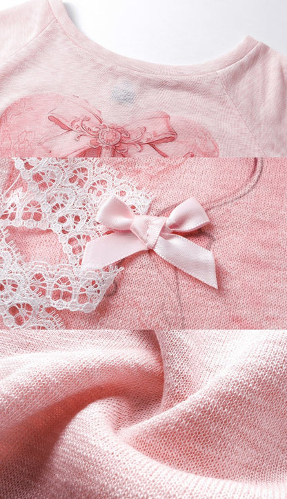 Close-up of a light pink knit garment with a matching pink satin bow, white lace trim, and a subtle heart motif on the chest.