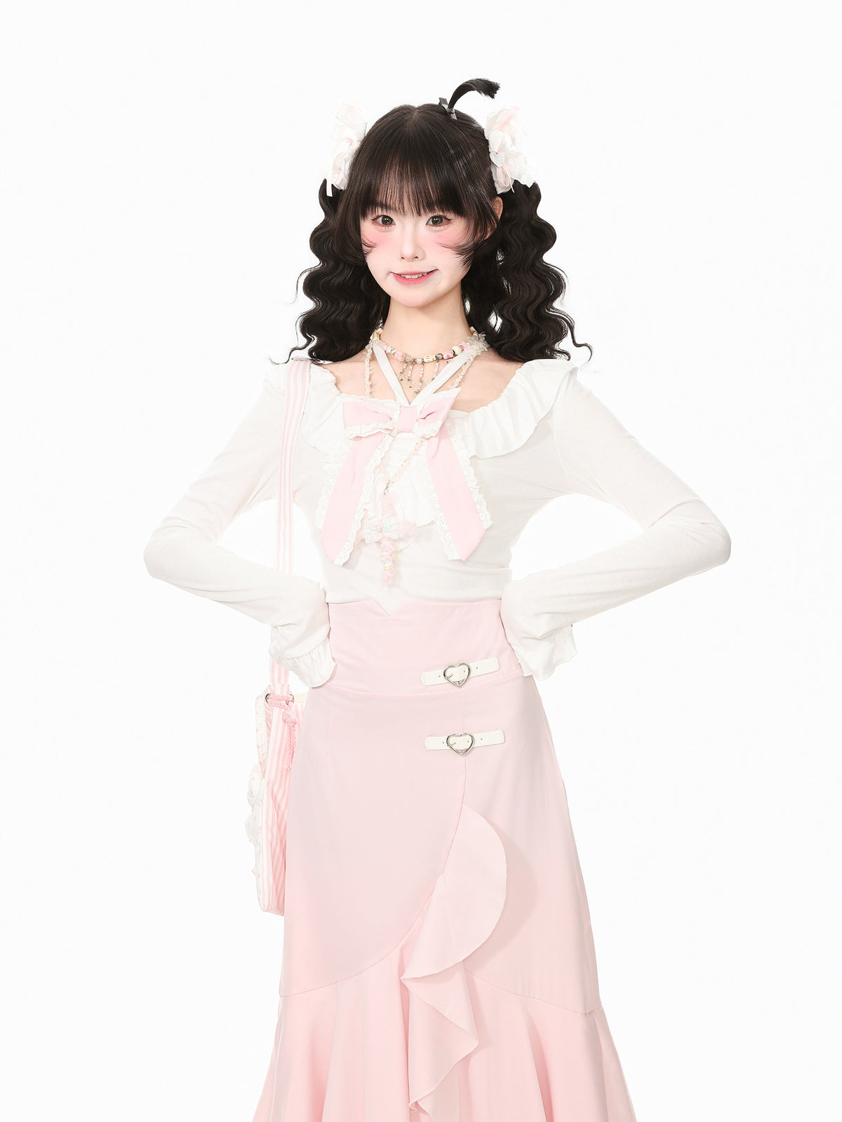 A young woman modeling a pastel pink and white Lolita-style outfit with a long-sleeve white top featuring a large pink bow, a high-waisted pink skirt with decorative buttons, and a matching pink bag, set against a plain white background.