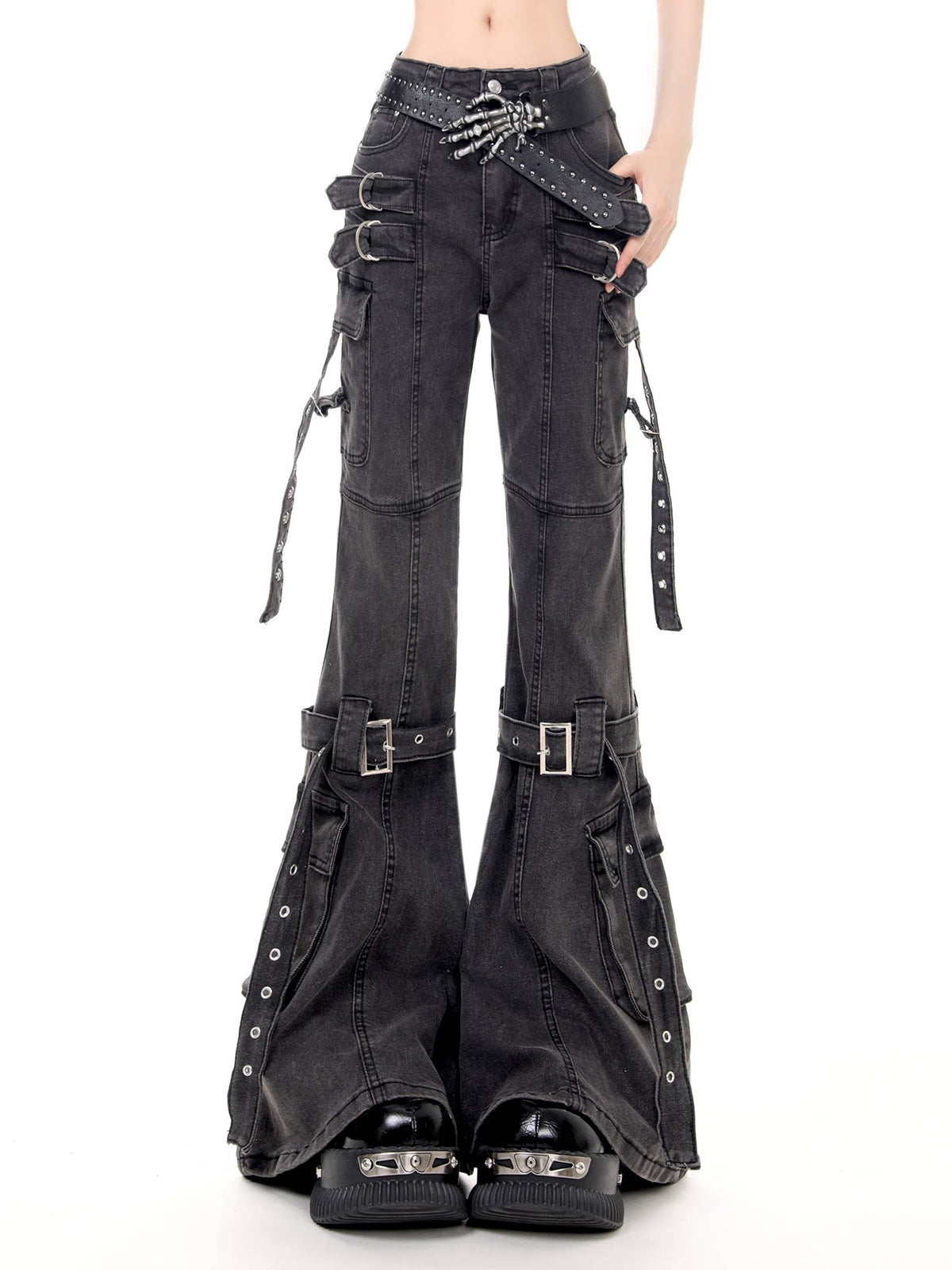 Black flared cargo pants with multiple buckle straps, side grommet details, and a studded belt, shown on a model against a white background.