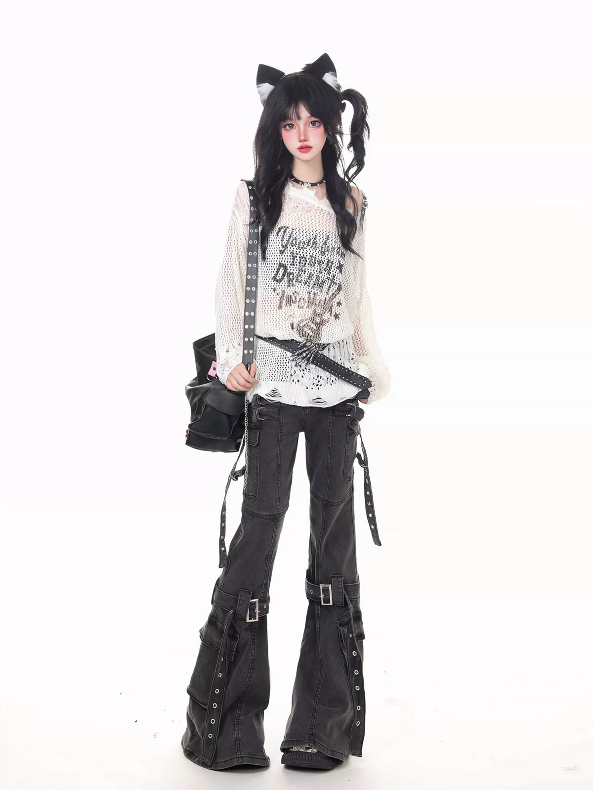 A model posing in a goth-style outfit featuring a white long-sleeve graphic t-shirt, black studded flare pants, a black studded shoulder bag, and a black cat-ear headband against a solid white background.