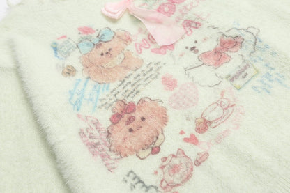 A close-up of a soft, pale pink plush blanket featuring cute teddy bear illustrations in pink, blue, and white, with a matching pink bow at the top.