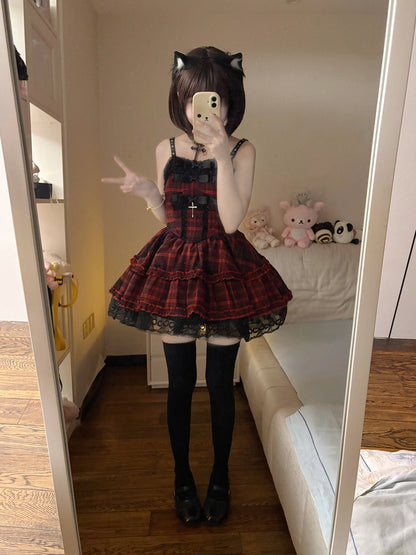 A person taking a mirror selfie in a bedroom, wearing a red and black plaid Lolita-style dress with a pleated skirt, black lace trim, black thigh-high stockings, and black shoes.
