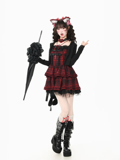 A model posing in a gothic Lolita-style outfit featuring a red and black plaid mini dress with a black long-sleeve top, holding a black umbrella against a solid white background.