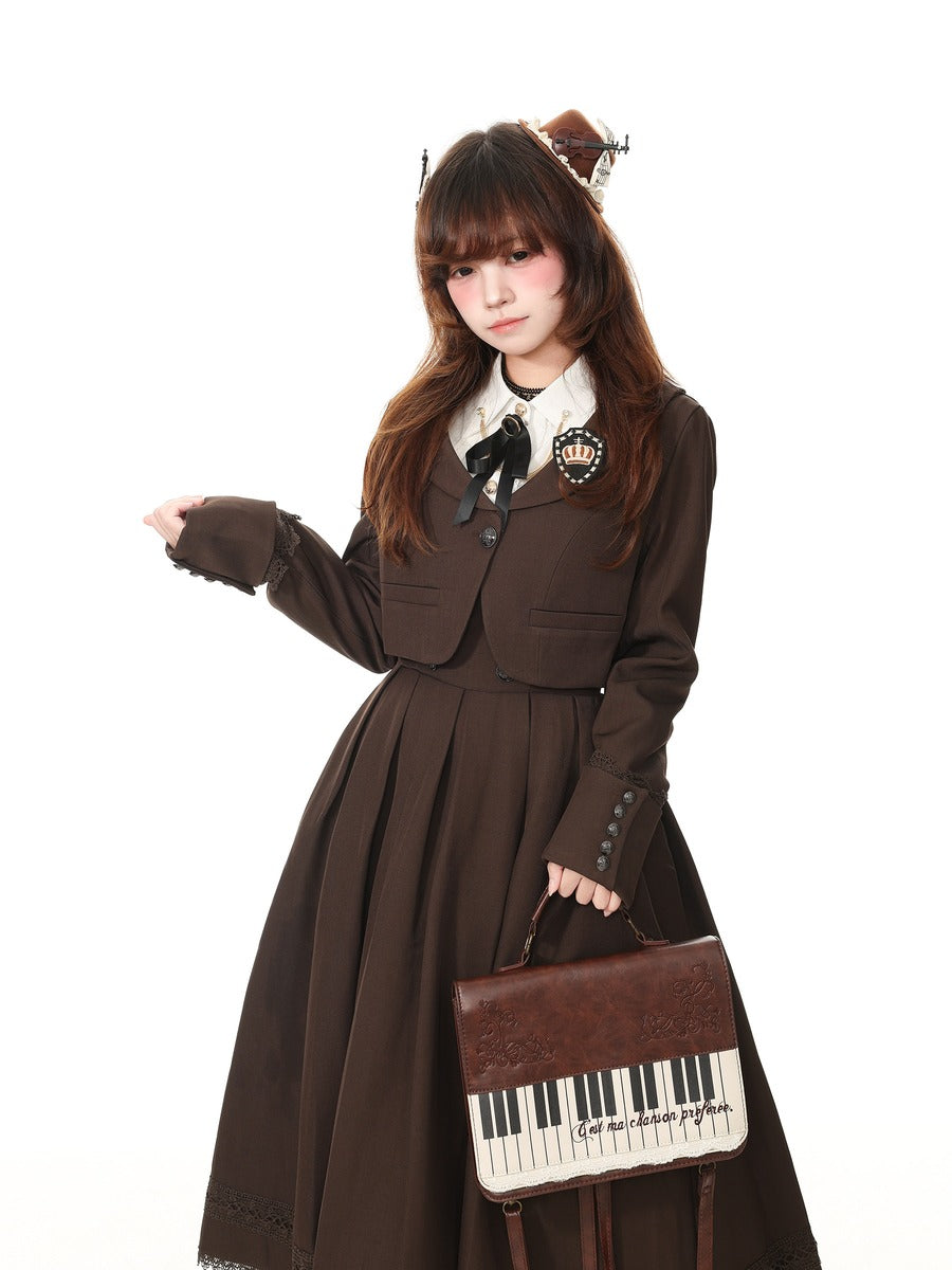 A young woman modeling a dark brown Victorian-style Lolita dress with a white collar, black bow, and decorative brooch, holding a brown briefcase with a piano keyboard design, set against a plain white background.