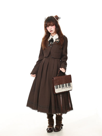 A model wearing a dark brown Victorian-style Lolita dress with a pleated skirt, matching cropped jacket, white collar, and a black bow. She is holding a brown piano-themed handbag and wearing brown knee-high boots against a solid white background.