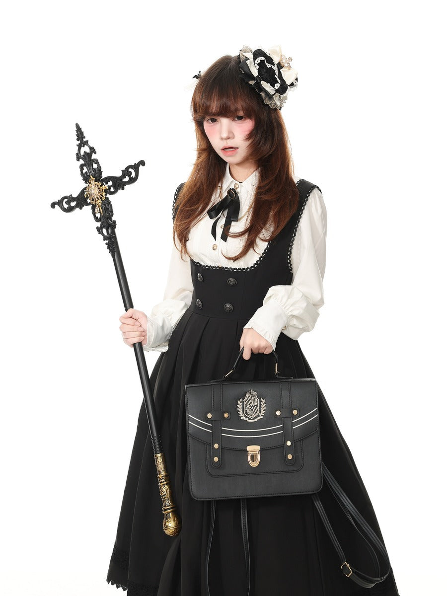 A woman modeling a black and white Victorian-style Lolita dress, holding a black decorative staff and a black leather briefcase with gold hardware against a solid white background.