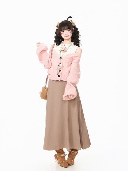 A young woman models a cute, pastel-colored outfit consisting of a light pink fuzzy cropped cardigan, a white ruffled collar blouse, a long taupe-brown skirt, and brown lace-up ankle boots. She is standing against a seamless white studio background.