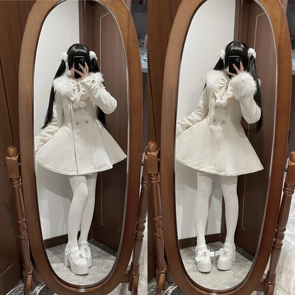 A person taking a mirror selfie wearing a cream-colored double-breasted coat with a fluffy collar, white tights, and white platform shoes, shown in front of a large wooden-framed floor mirror.