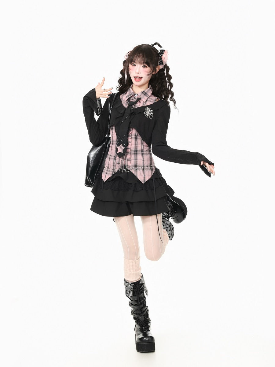 A model posing in a black goth-style school uniform outfit with a pink plaid shirt, black cardigan, pleated skirt, thigh-high stockings, and black platform boots against a solid white background.