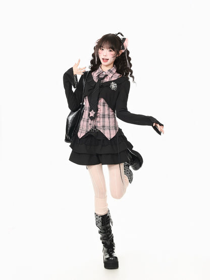 A model posing in a black goth-style school uniform outfit with a pink plaid shirt, black cardigan, pleated skirt, thigh-high stockings, and black platform boots against a solid white background.
