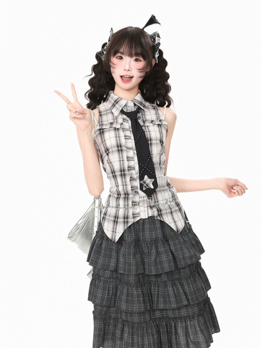 A young woman posing in a sleeveless plaid vest with a black star-patterned tie, paired with a tiered dark gray plaid skirt, against a solid white background.