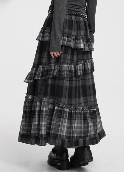 A black and gray plaid tiered maxi skirt with ruffled layers, styled with a dark gray long-sleeve top and black platform boots against a plain white studio background.