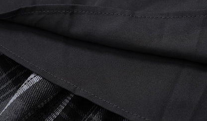 Close-up of a black fabric garment with visible stitching, showing part of a black-and-white plaid pattern underneath.