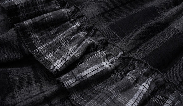 Close-up of a black and gray plaid fabric with gathered ruffles, showing the texture and pattern details.