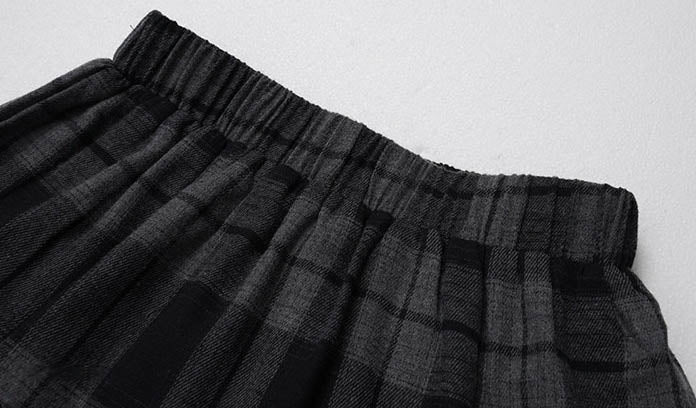Close-up of a black and gray plaid pleated skirt with an elastic waistband, laid flat on a light gray background.