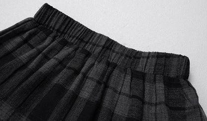 Close-up of a black and gray plaid pleated skirt with an elastic waistband, laid flat on a light gray background.