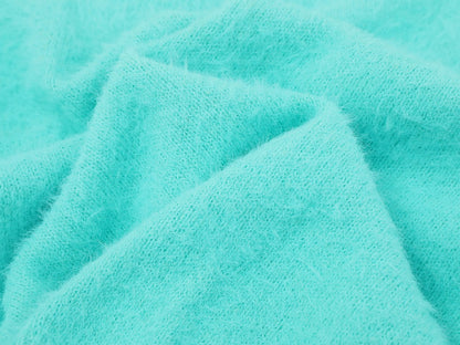 A close-up of soft, fuzzy knit fabric in a bright aqua or turquoise color, draped in gentle folds to show texture.