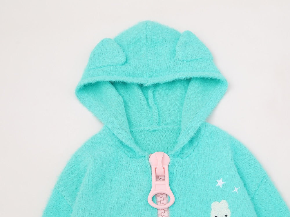 A close-up of a mint green fuzzy hooded sweatshirt with a pink zipper pull and small white star details on the front, set against a plain light background.