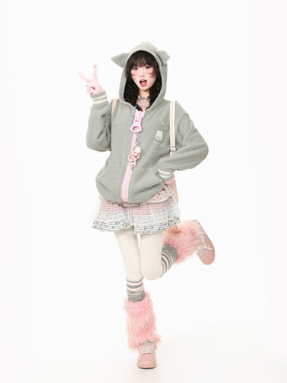 A model posing in a light gray cat-ear hooded sweatshirt with a pink zipper and cute accessories, paired with a patterned pleated skirt, pink fuzzy socks, and pink boots, set against a plain white background.