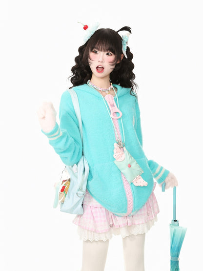 A young woman modeling a pastel anime-inspired outfit against a plain white background. She is wearing a light blue hooded sweatshirt with pink trim, a pink and white plaid pleated skirt, white thigh-high socks, a matching light blue crossbody bag, and a small white headband with a cherry accent.
