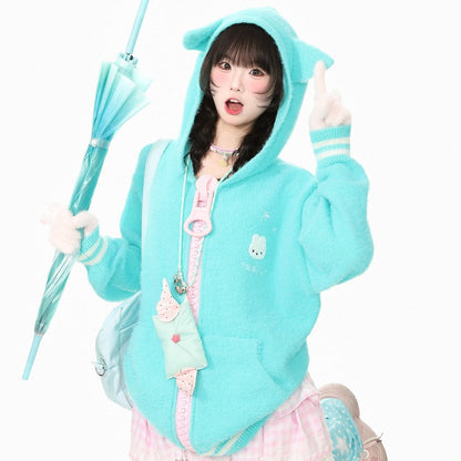 A model wearing a light blue fuzzy hooded sweatshirt with cat ears on the hood, holding a matching light blue umbrella against a solid white background.