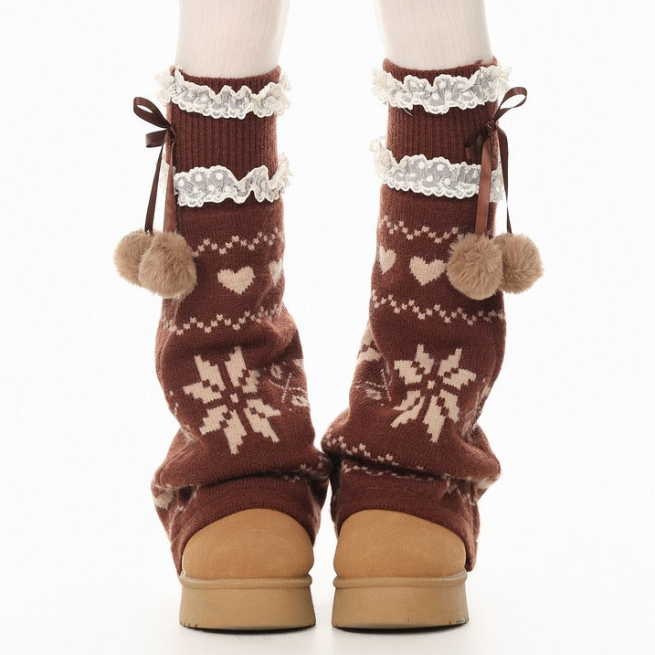 Brown knit leg warmers with cream snowflake and heart patterns, white lace trim, and pom-pom details, shown on a white background.