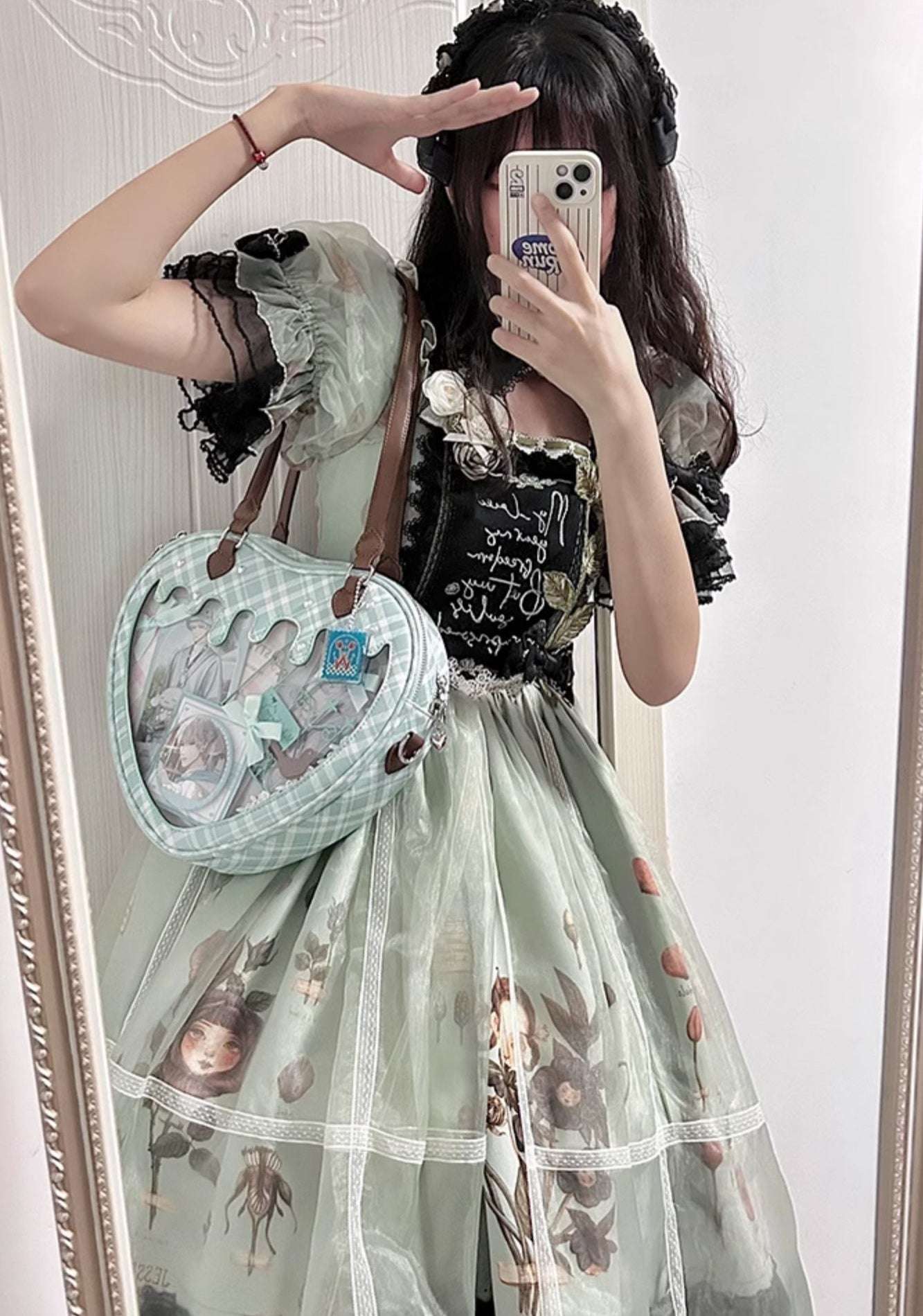Person wearing a floral dress and holding a heart-shaped bag in front of a mirror.