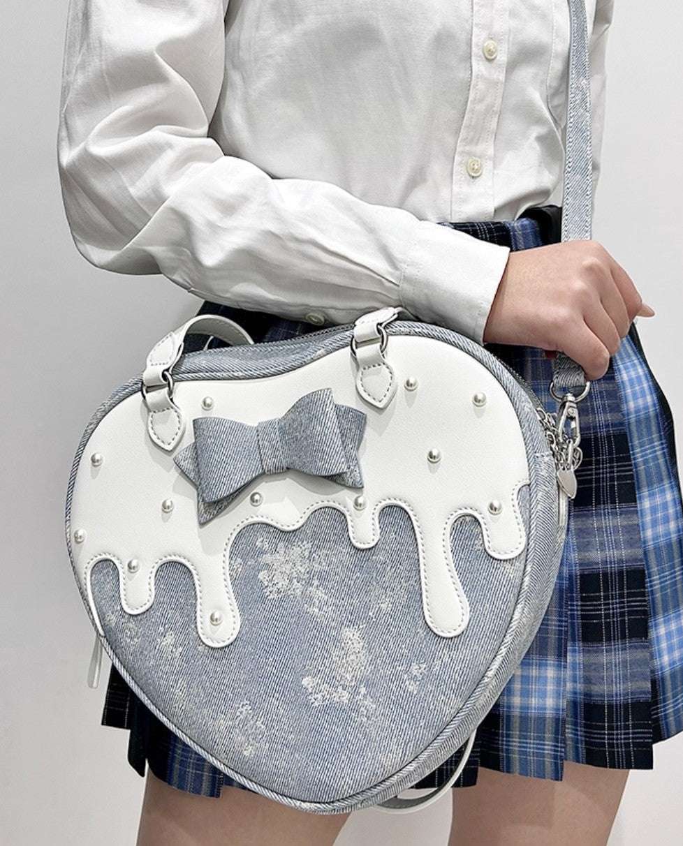 Heart-shaped bag with a bow design held by a person wearing a white shirt and plaid skirt.