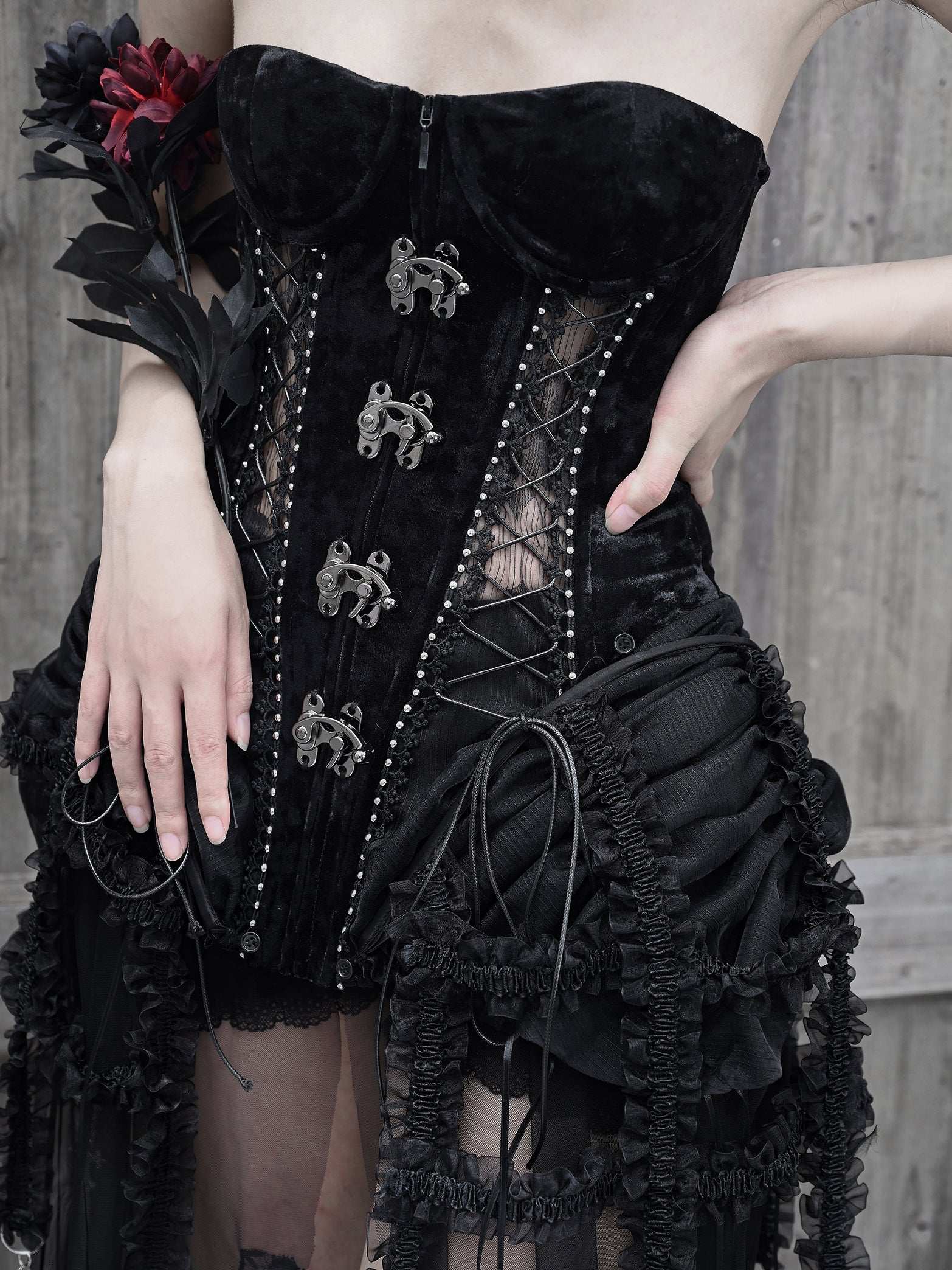 Black corset with intricate detailing worn by a person against a wooden background