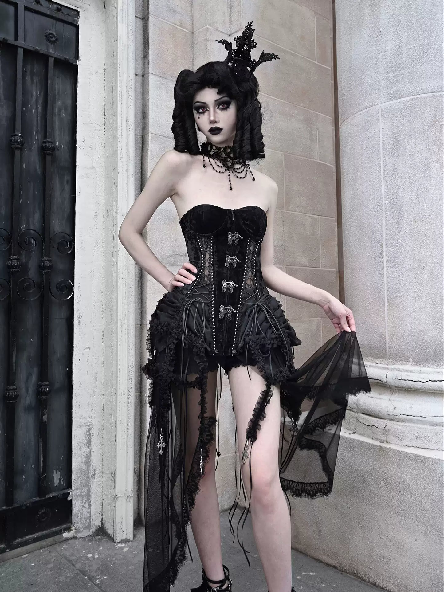 Person wearing a black gothic-style dress with sheer elements in an urban setting.