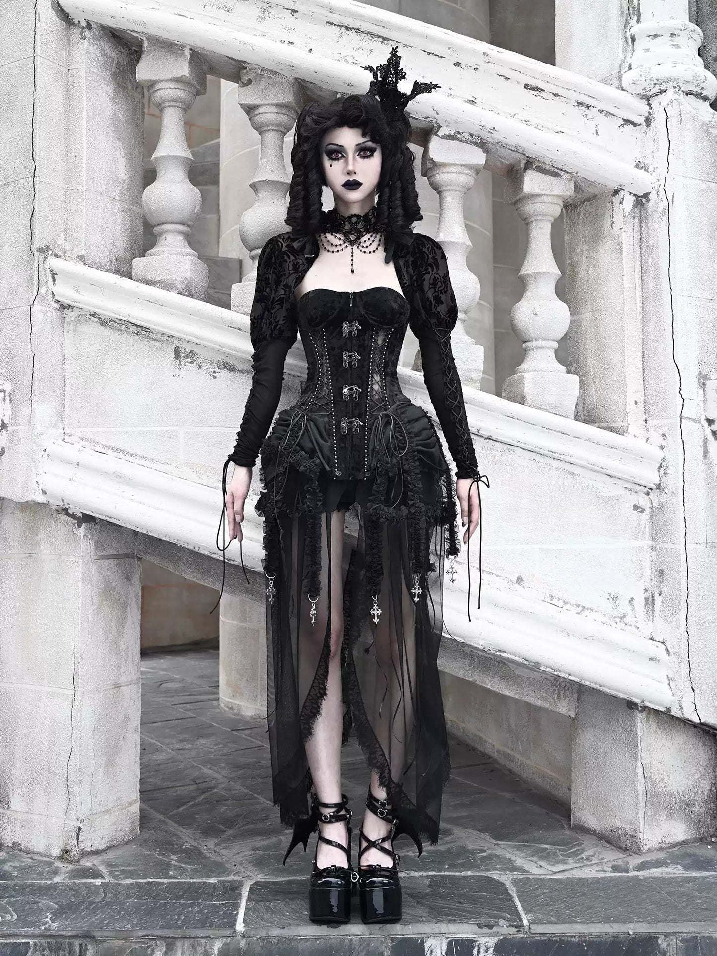 Person wearing a black gothic outfit standing on stone steps.