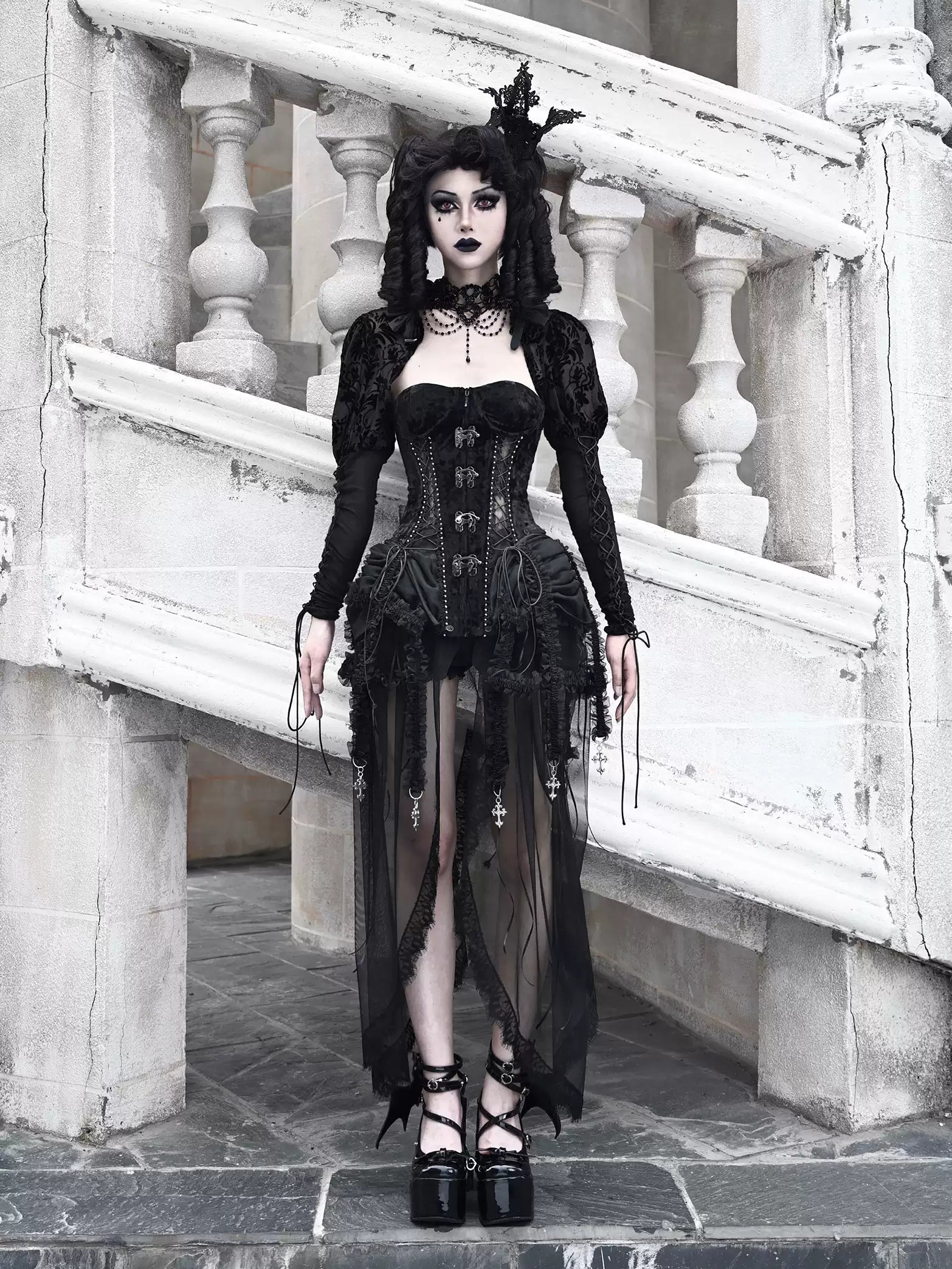 Person wearing a black gothic outfit standing on stone steps.