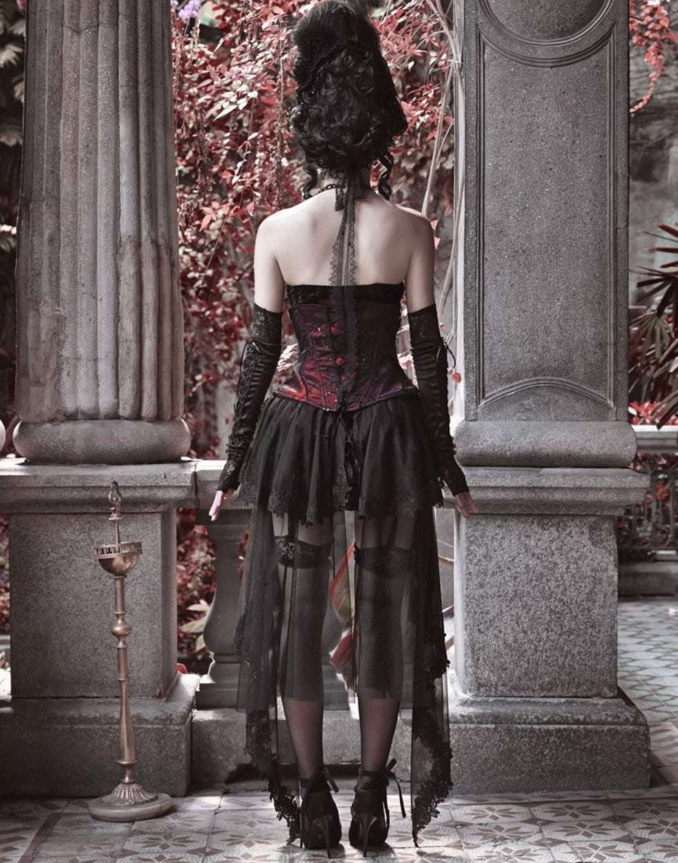 Person wearing a gothic-style dress standing between stone columns with red foliage in the background