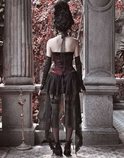 Person wearing a gothic-style dress standing between stone columns with red foliage in the background